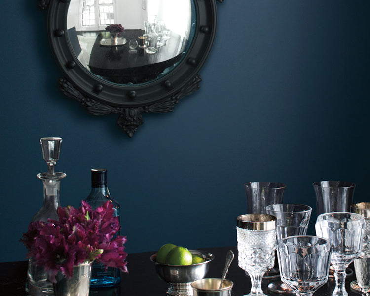 A dark blue-painted dining room wall frames ornate glasses on a table.